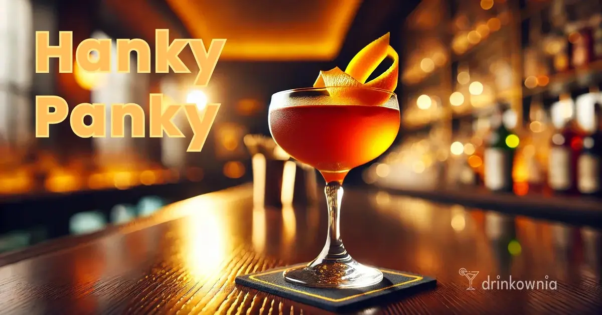 Drink Hanky Panky o bursztynowym kolorze w kieliszku coupe, udekorowany skórką pomarańczy, serwowany na eleganckim barze